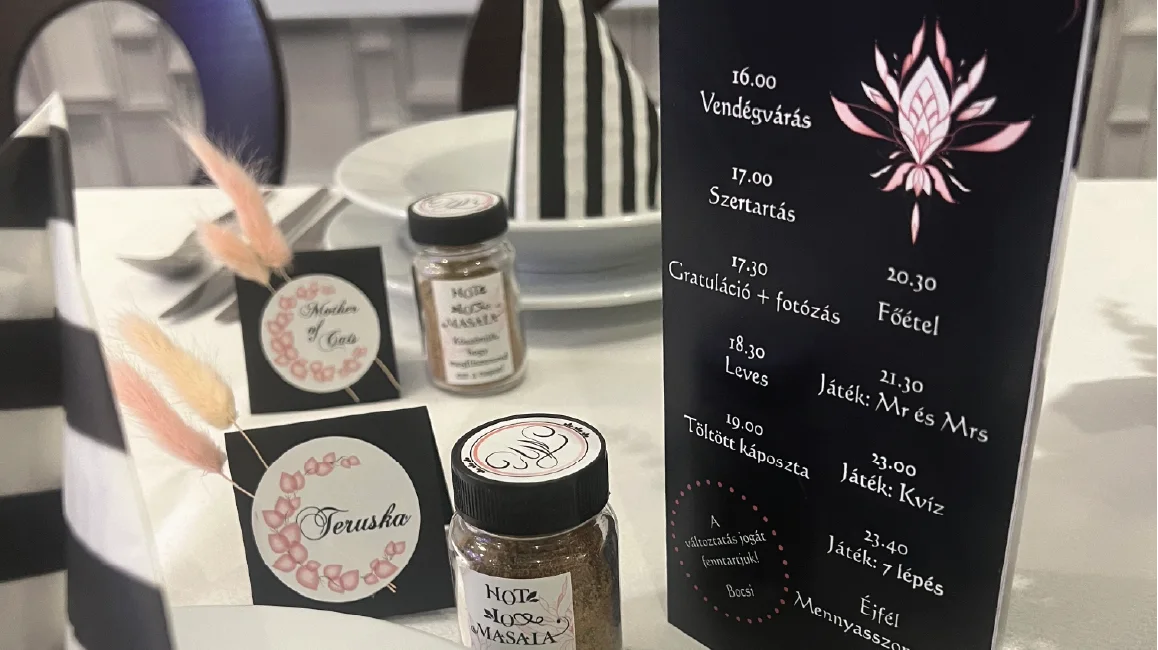 Egyedi esküvői grafika: fekete menükártya, ültetőkártyák és köszönőajándék címkék egy terített asztalon.